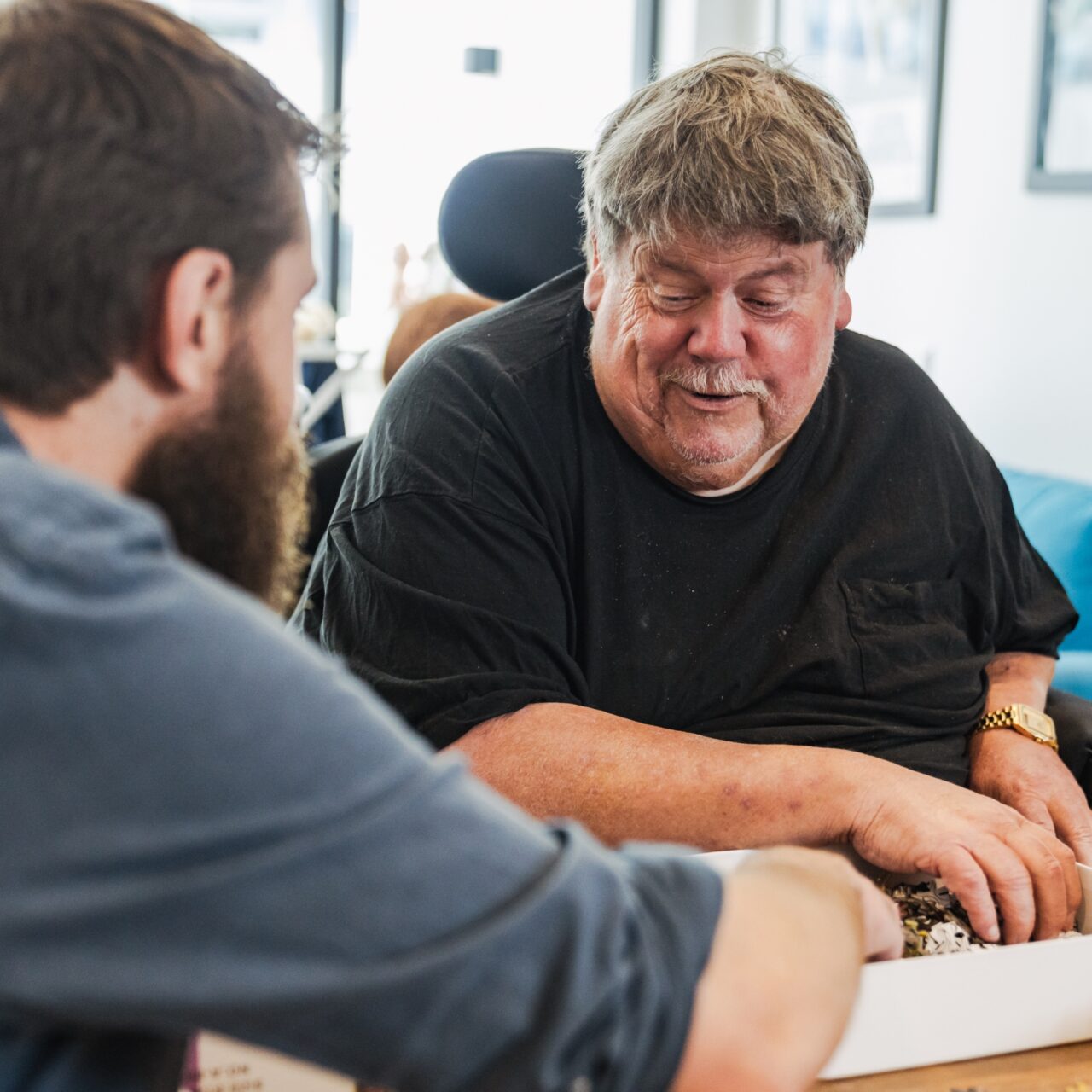 A support worker and an older participant sharing a moment over a puzzle